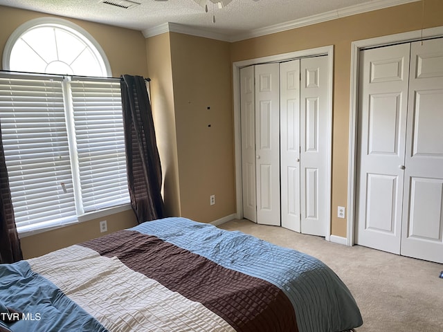 bedroom featuring light carpet, visible vents, baseboards, two closets, and ornamental molding