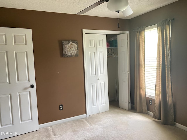 unfurnished bedroom with a textured ceiling, baseboards, light colored carpet, a closet, and ceiling fan