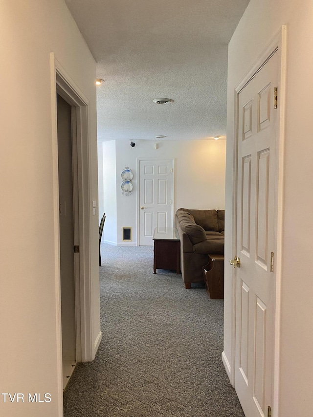 corridor with dark colored carpet, visible vents, and a textured ceiling