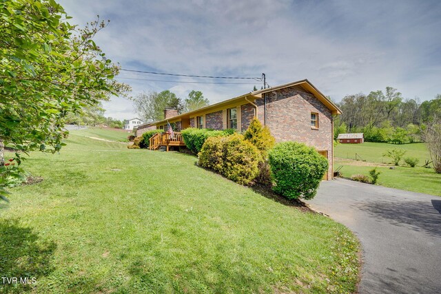 view of property exterior featuring a chimney, aphalt driveway, a yard, a garage, and brick siding
