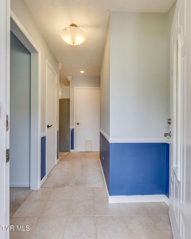 hallway featuring baseboards, tile patterned floors, and carpet