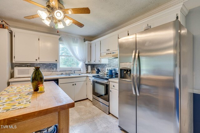 kitchen featuring a sink, appliances with stainless steel finishes, light countertops, under cabinet range hood, and ornamental molding