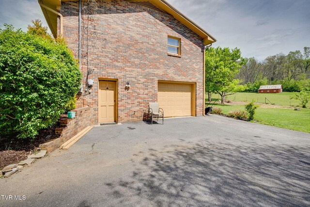 view of home's exterior featuring an attached garage, driveway, brick siding, and a yard