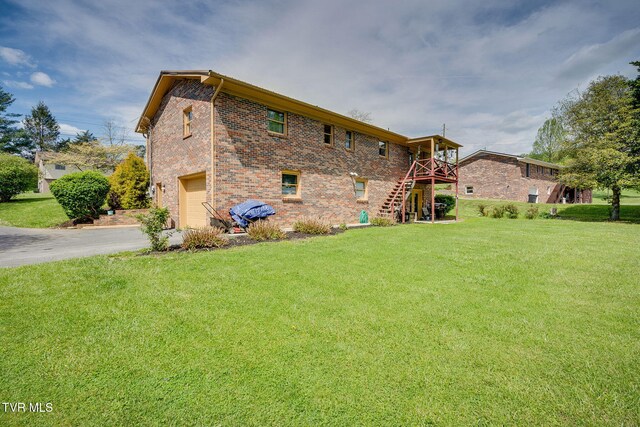 rear view of property featuring a lawn, an attached garage, driveway, and stairs