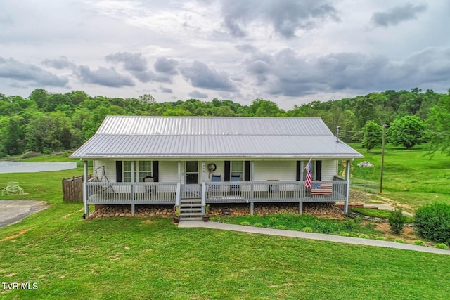 country-style home featuring covered porch, a wooded view, metal roof, and a front yard