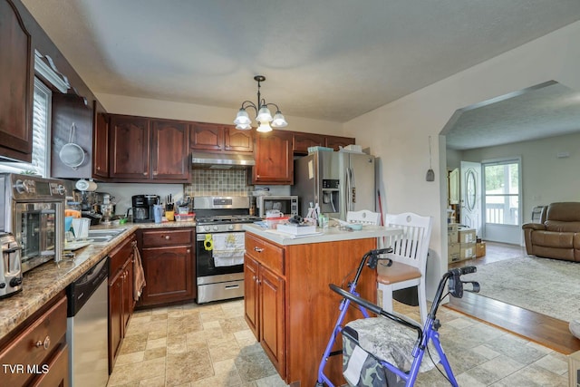 kitchen featuring under cabinet range hood, stainless steel appliances, arched walkways, and stone finish floor