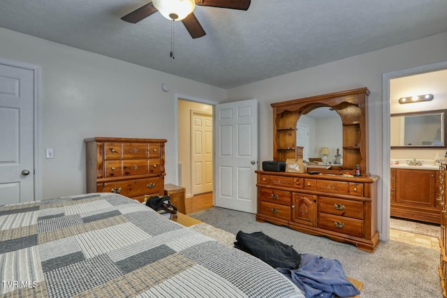 bedroom with ceiling fan, light colored carpet, a sink, and ensuite bath