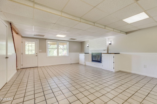 112 Fairwood St, Kingsport, TN 37660 - unfurnished living room featuring wainscoting, a brick fireplace, light tile patterned floors, and a drop ceiling