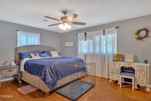 bedroom with ceiling fan, wood finished floors, and multiple windows