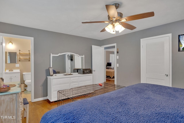 bedroom featuring wood finished floors, baseboards, ceiling fan, a sink, and ensuite bath