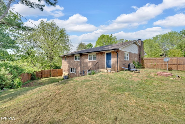 back of property with a fenced backyard, a chimney, brick siding, entry steps, and a lawn