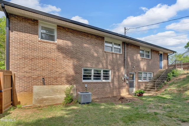 rear view of property with fence, stairs, brick siding, central air condition unit, and a yard