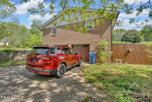 view of property exterior featuring brick siding, an attached garage, fence, and concrete driveway