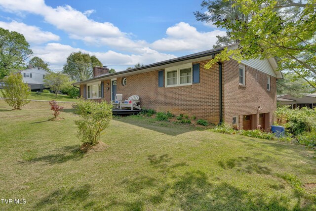 exterior space with an attached garage, a chimney, a front yard, and brick siding