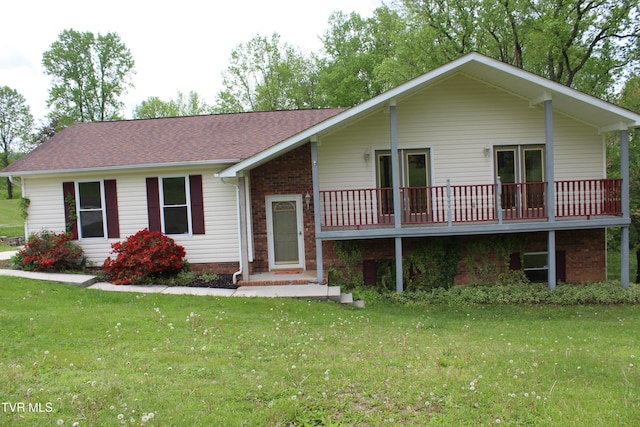 view of front of home with brick siding, a front lawn, roof with shingles, and a deck