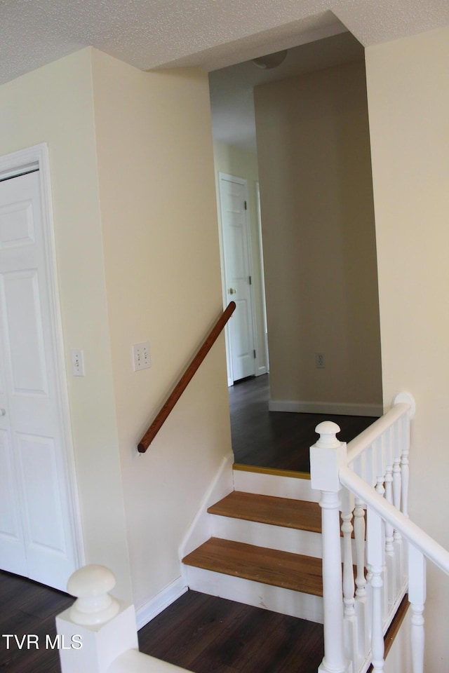 staircase with baseboards, wood finished floors, and a textured ceiling