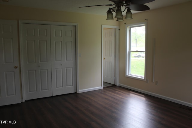 unfurnished bedroom with baseboards, multiple windows, dark wood-type flooring, and a closet