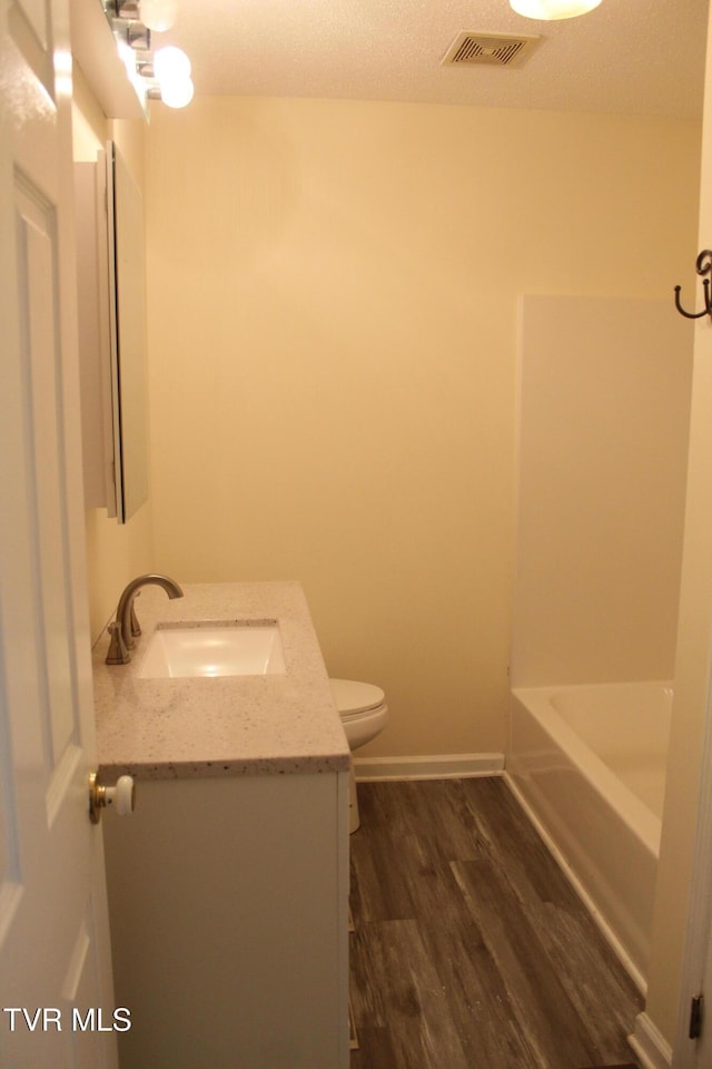 full bath featuring wood finished floors, visible vents, toilet, vanity, and baseboards