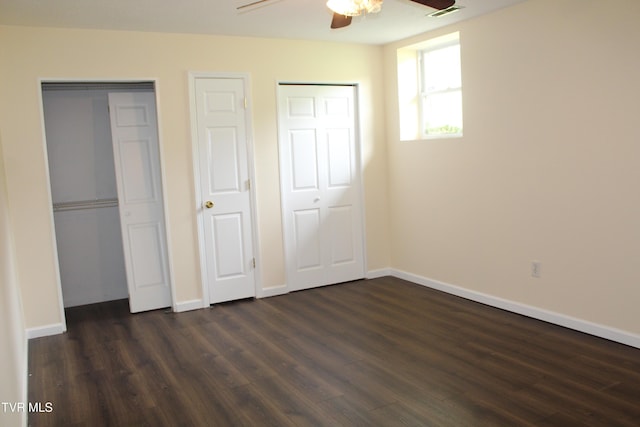 unfurnished bedroom with baseboards, multiple closets, and dark wood-style floors