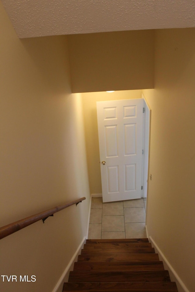 stairs featuring tile patterned flooring, baseboards, and a textured ceiling
