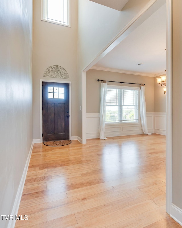foyer with an inviting chandelier, crown molding, wood finished floors, and plenty of natural light