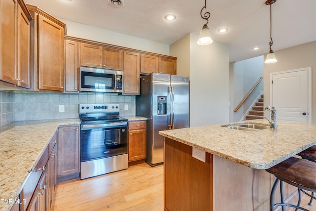 kitchen featuring brown cabinets, a sink, light stone countertops, light wood-style flooring, and appliances with stainless steel finishes