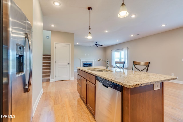 kitchen featuring hanging light fixtures, a sink, brown cabinetry, stainless steel appliances, and a fireplace