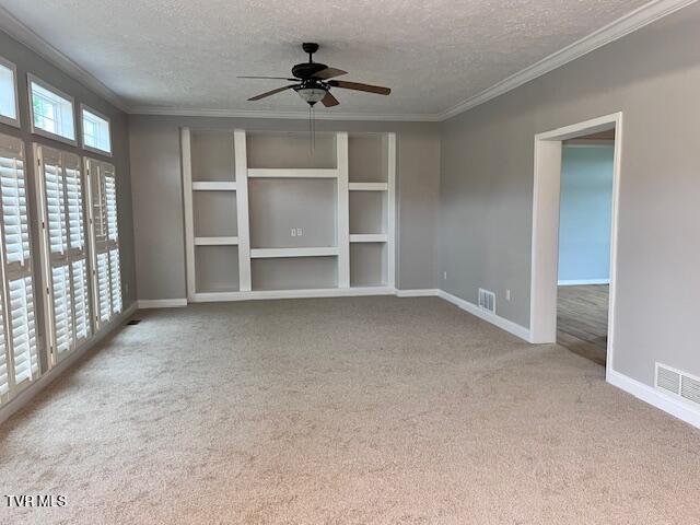 carpeted empty room featuring a textured ceiling, baseboards, ornamental molding, and visible vents