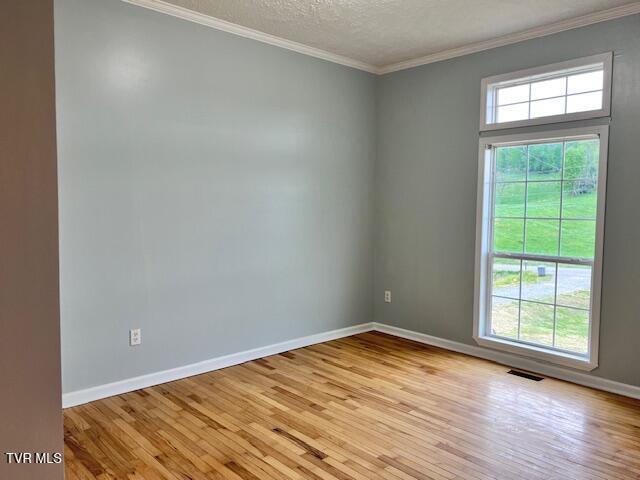 empty room featuring visible vents, light wood finished floors, baseboards, and ornamental molding