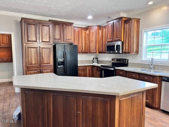 kitchen featuring crown molding, appliances with stainless steel finishes, light wood finished floors, and a sink