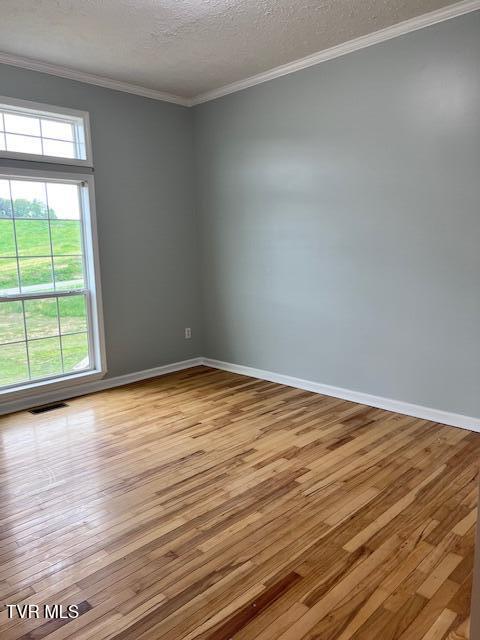 unfurnished room with a textured ceiling, baseboards, visible vents, crown molding, and hardwood / wood-style flooring