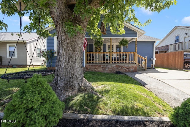 view of property hidden behind natural elements featuring a porch, fence, and a front lawn