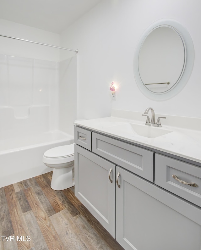 bathroom featuring toilet, vanity, wood finished floors, and shower / washtub combination