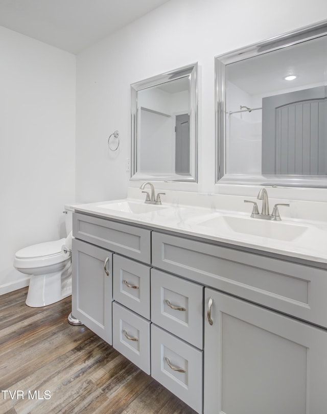 bathroom featuring toilet, double vanity, wood finished floors, and a shower