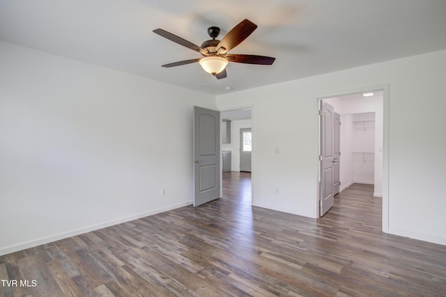 unfurnished bedroom with wood finished floors, a walk in closet, baseboards, and ceiling fan