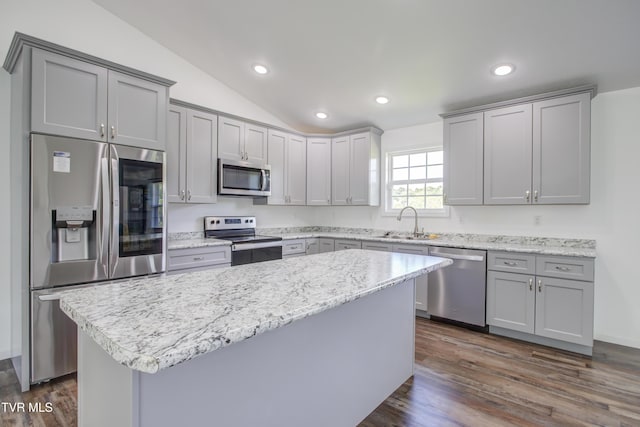 kitchen with appliances with stainless steel finishes, gray cabinetry, a sink, lofted ceiling, and a center island