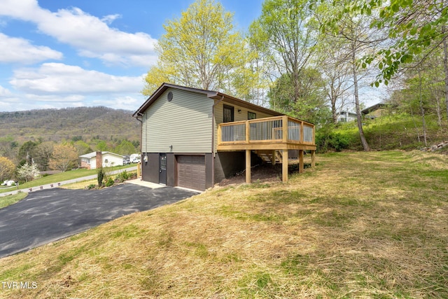 exterior space with a lawn, driveway, an attached garage, and a deck with mountain view
