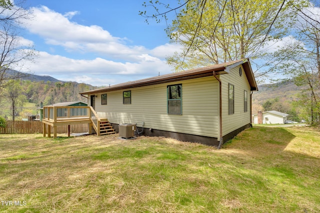 back of house with a deck with mountain view, fence, central AC unit, and a lawn