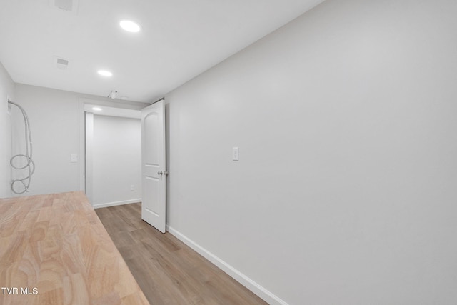 corridor with light wood finished floors, recessed lighting, visible vents, and baseboards
