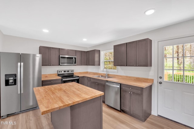 kitchen featuring appliances with stainless steel finishes, wooden counters, dark brown cabinets, light wood finished floors, and a sink