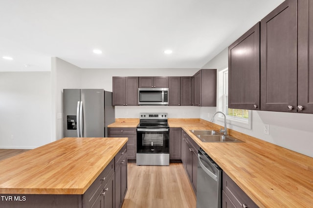 kitchen featuring a sink, wood counters, light wood-type flooring, dark brown cabinetry, and appliances with stainless steel finishes