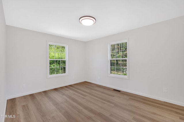 unfurnished room featuring wood finished floors, a healthy amount of sunlight, visible vents, and baseboards