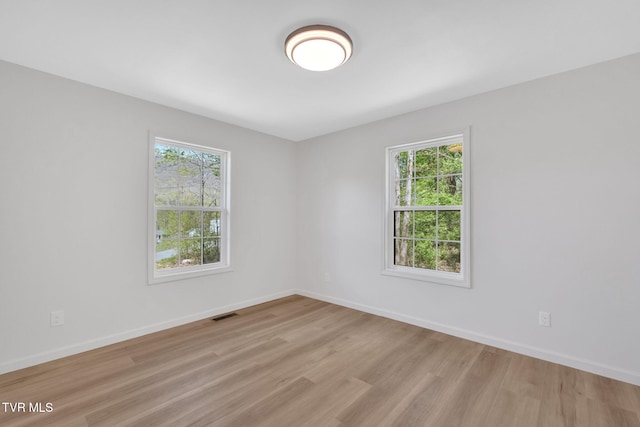 empty room with light wood finished floors, visible vents, a wealth of natural light, and baseboards