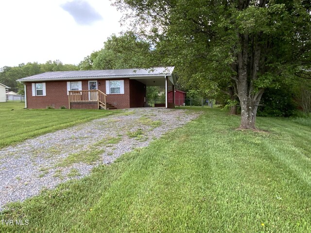 single story home featuring brick siding, metal roof, a carport, driveway, and a front lawn
