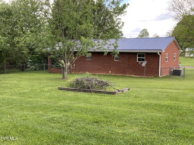rear view of house featuring brick siding, fence, metal roof, and a lawn