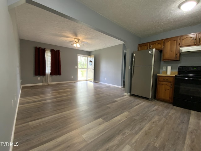 kitchen with black electric range, a textured ceiling, under cabinet range hood, and freestanding refrigerator