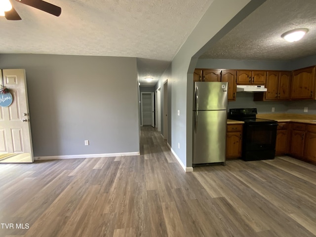kitchen with a textured ceiling, freestanding refrigerator, under cabinet range hood, black electric range, and wood finished floors