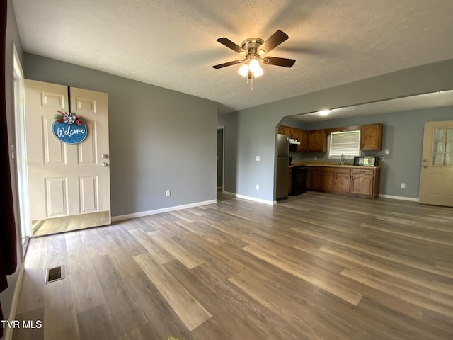unfurnished living room featuring arched walkways, wood finished floors, ceiling fan, visible vents, and a textured ceiling