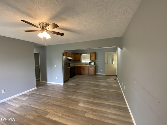 unfurnished living room featuring a sink, a textured ceiling, a ceiling fan, and dark wood-style flooring