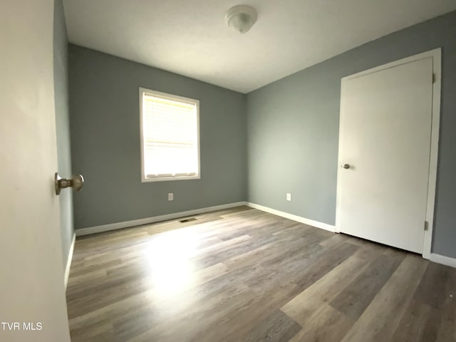 spare room with wood finished floors, visible vents, and baseboards